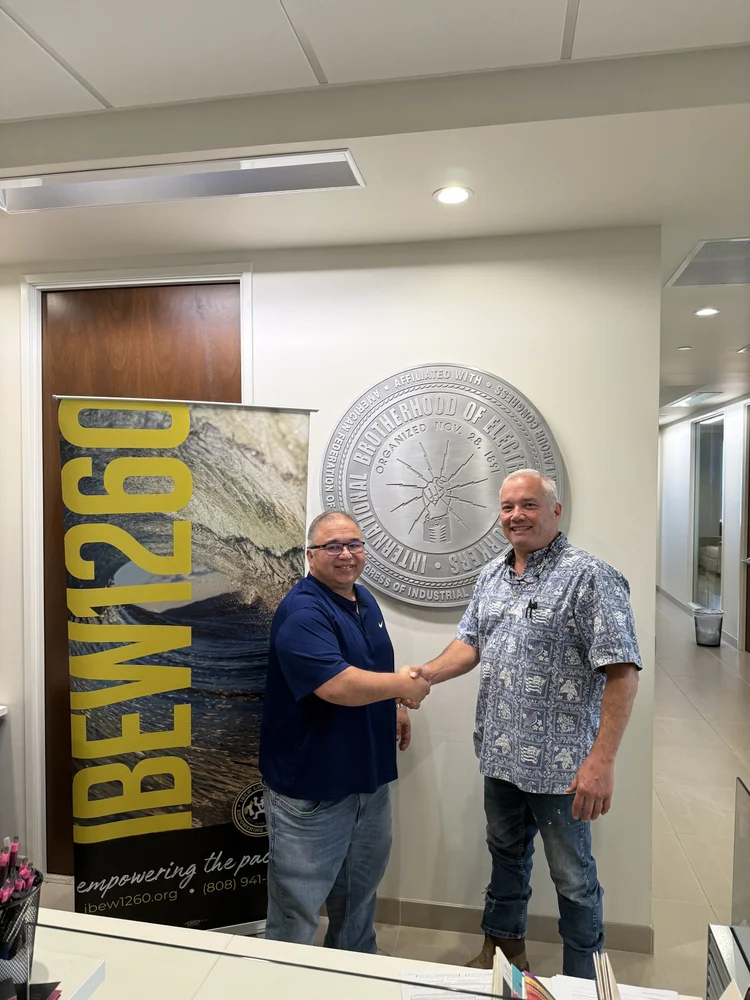 Two men shaking hands in front of a wall with an insignia and a banner for IBEW Local 1260.